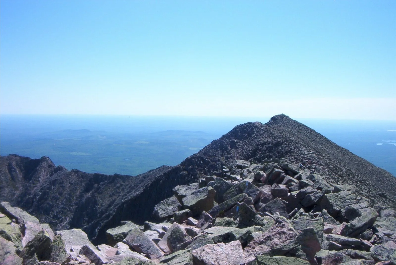 Looking east along the Knife Edge arête toward Pamola Peak — a tiny hiker visible on the narrow ridge, northern Maine wilderness stretching flat to the north
